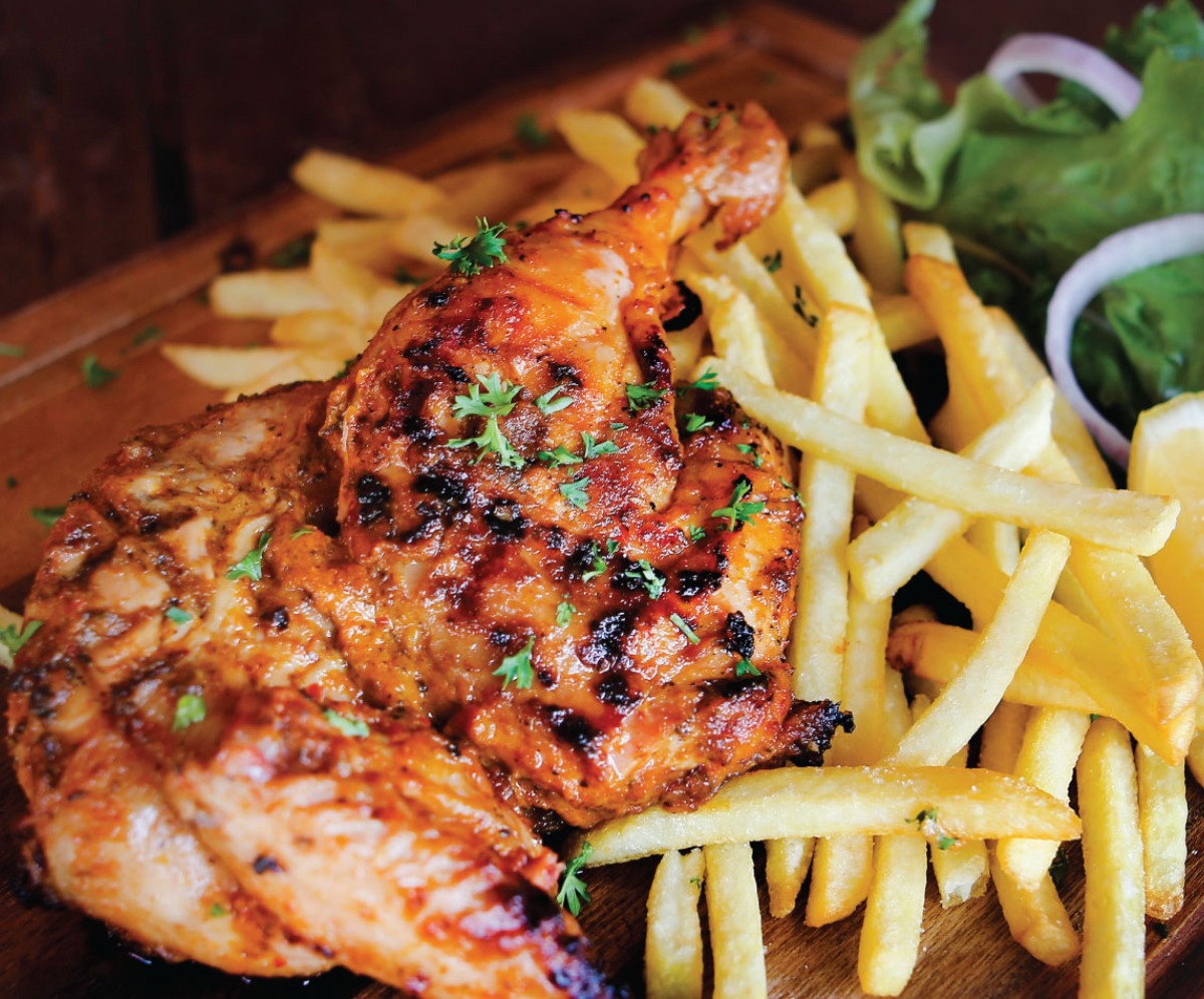 wooden board filled with peri peri chicken, fries and a green salad