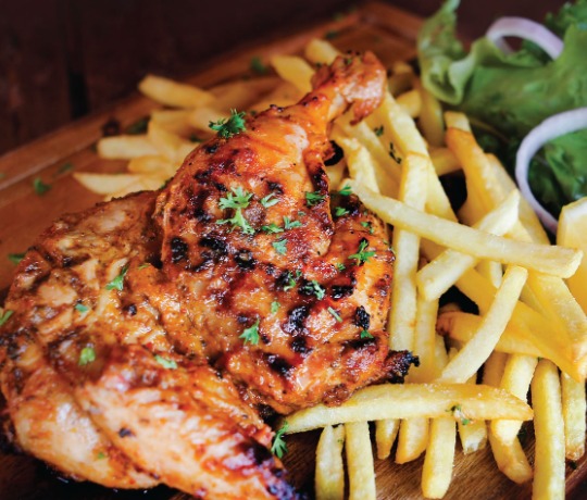 wooden board filled with a peri peri chicken, with chips and green salad