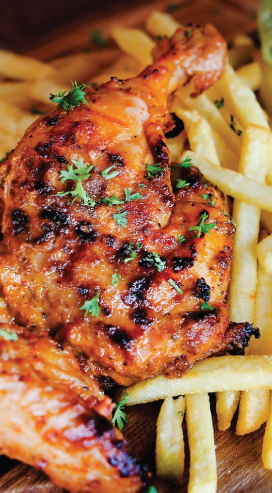 Close up of marinated peri peri chicken leg, with grill marks and garnished with parsley, chips on the side
